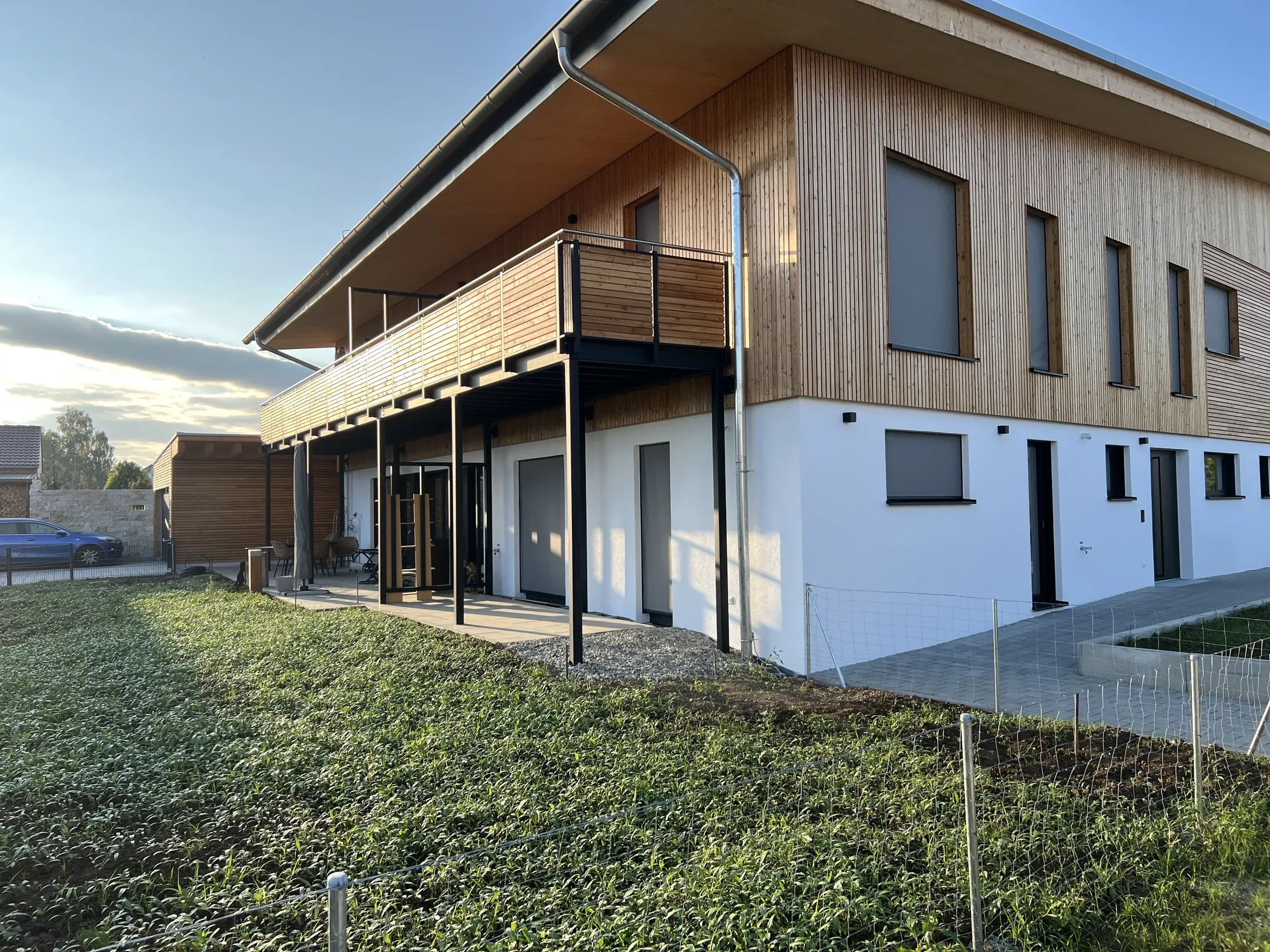 Obergeschoss mit senkrechter Holzschalung, weiß verputztem Erdgeschoss und Balkon mit Holzbrüstung auf Stahlstützen