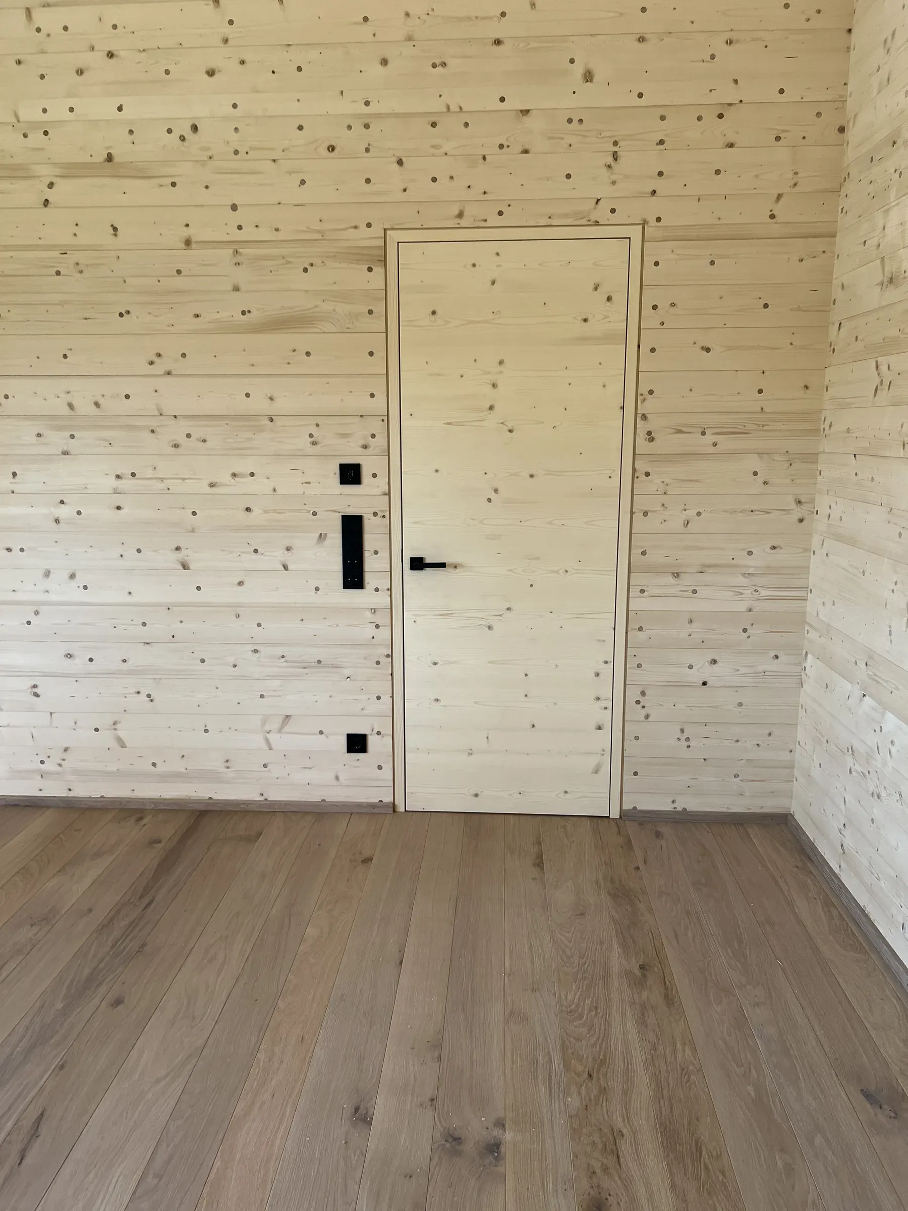 Flächenbündig in eine Holzwand gesetzte helle Holz-Innentür mit schwarzem Drücker über einem Dielenboden