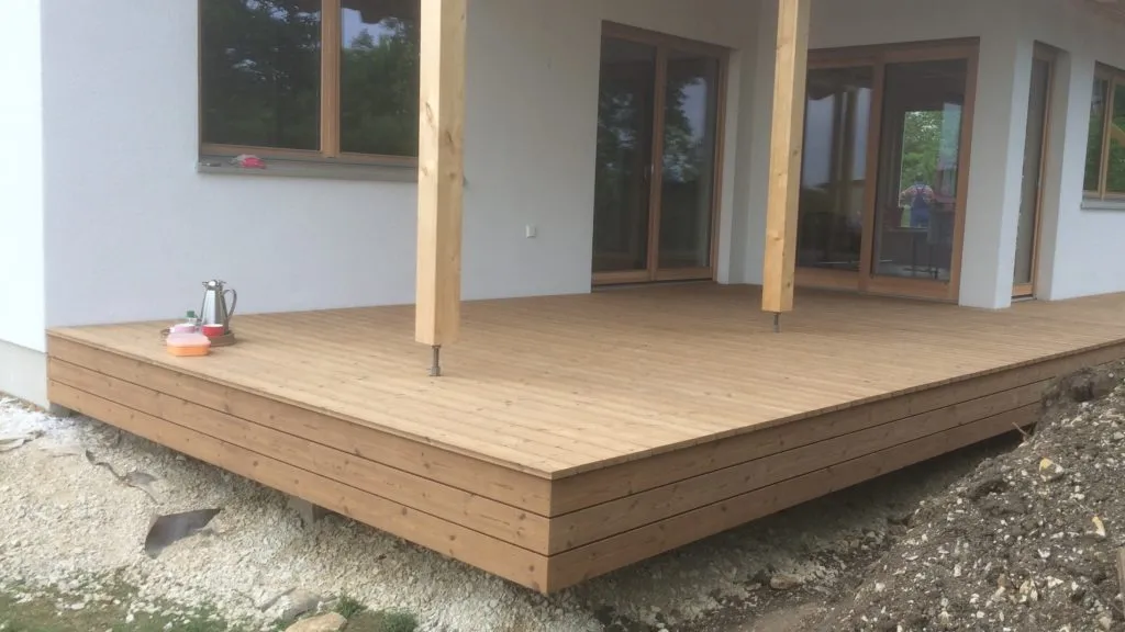 Neu gebaute Holzterrasse am Haus mit hölzernen Dachstützen und Terrassentüren mit Holzrahmen