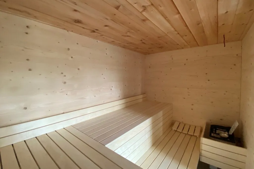 Innenraum einer Sauna mit hellen Holzpaneelen an Wänden und Decke sowie stufenförmigen Sitzbänken
